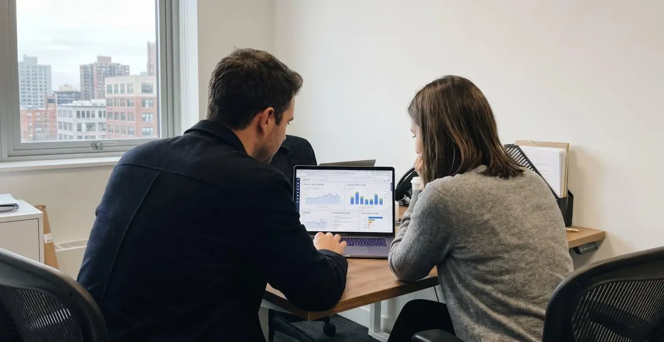 Two marketing professionals reviewing SEO performance analytics on laptop in modern office with natural window lighting